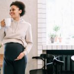 Pregnant woman enjoying a peaceful moment with a mug, surrounded by plants indoors.