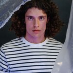 Portrait of a young man with curly hair in a striped shirt, with artistic plastic background.