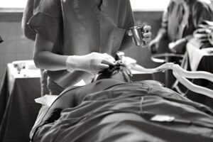 Black and white image of a medical professional performing a procedure in an operating room.