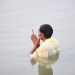 A man standing in waist-deep water with hands in prayer at dawn, symbolizing spiritual devotion.