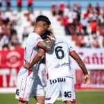 Two soccer players celebrating a goal with a crowd in the background.