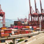 A vibrant view of Hong Kong's bustling shipping port with red cranes and stacked containers.