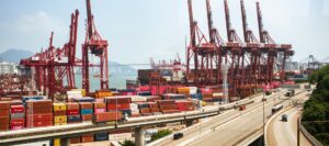 A vibrant view of Hong Kong's bustling shipping port with red cranes and stacked containers.