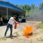 A man uses a fire extinguisher to put out a controlled fire during an outdoor safety training session.