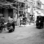 Black and white photo of a busy street in Delhi with rickshaws and pedestrians.
