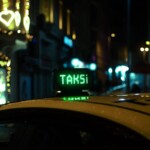 A taxi with a glowing 'TAKSİ' sign in a bustling nighttime city street adorned with heart-shaped lights.