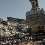 Powerful excavator clearing earthquake debris amidst building ruins in Antakya, Turkey.