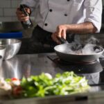 Chef prepares food in a sleek kitchen using a frying pan on an induction cooktop.