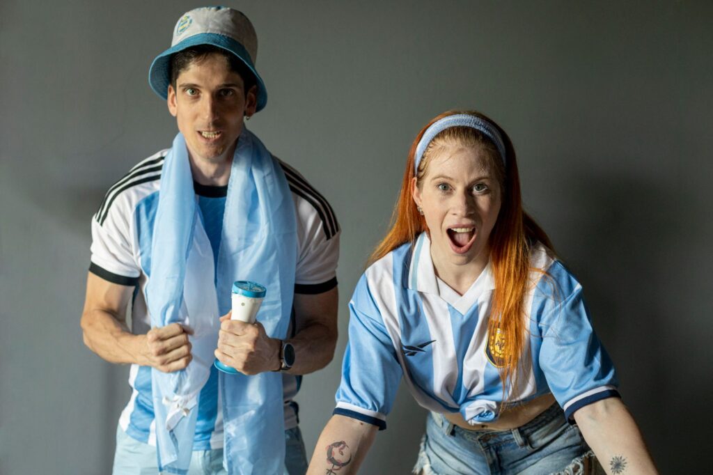 Two excited fans in Argentina jerseys express joy and support indoors.