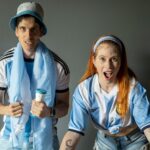 Two excited fans in Argentina jerseys express joy and support indoors.