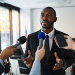 Confident businessman answering questions from the media during a press conference indoors.