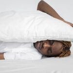 A man enjoying a peaceful nap indoors under a white pillow, conveying relaxation.