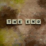Scrabble tiles forming 'The End' on a textured rustic background, conveying closure.