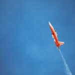 Red jet performing aerobatic flight against clear blue sky, showcasing precision and speed.