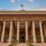 Government building in New Delhi featuring columns and an Indian flag under a vibrant sky.