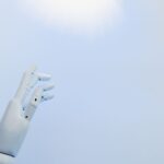 A robotic hand reaching towards a bright light on a white background symbolizing innovation.
