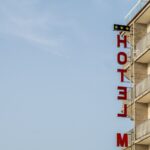 A modern hotel building with distinct balconies and a red sign against a clear blue sky.