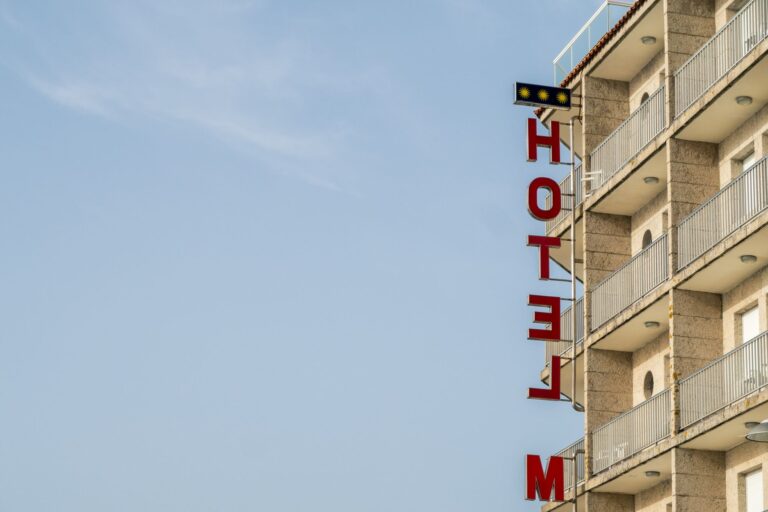 A modern hotel building with distinct balconies and a red sign against a clear blue sky.