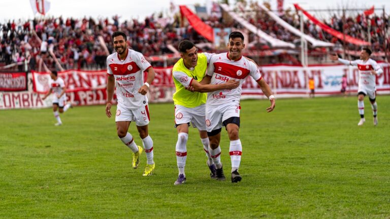 Football players celebrating on the field with an enthusiastic crowd in the background.