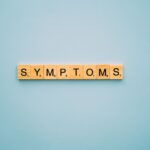 Scrabble tiles spelling 'SYMPTOMS' on a blue background, symbolizing health concepts.