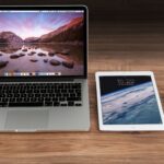Modern workspace showcasing Apple laptop, tablet, and smartphone on a wooden desk.