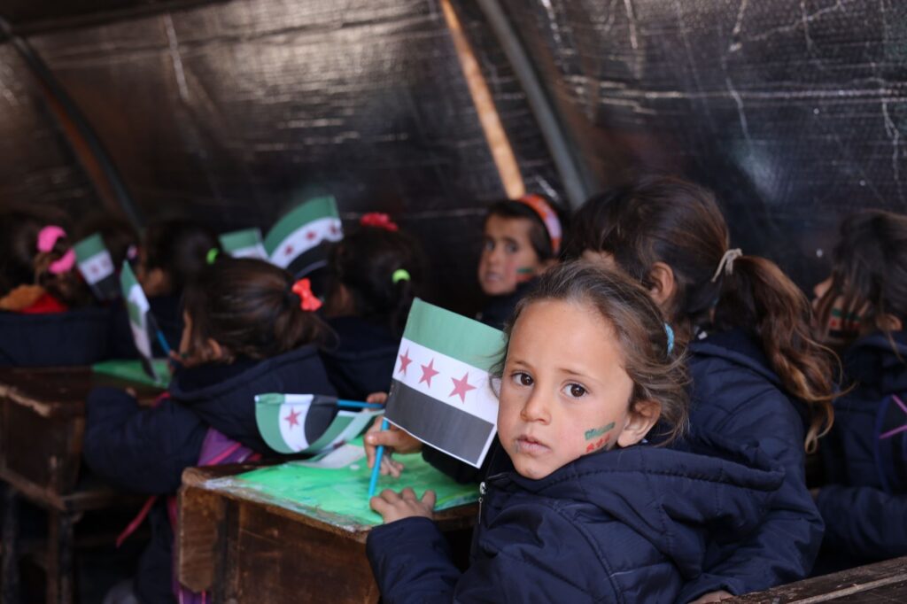 Children holding Syrian flags in a classroom symbolize hope and unity.