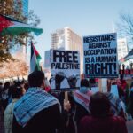 A city rally with protesters holding signs promoting Palestinian rights and human rights advocacy.