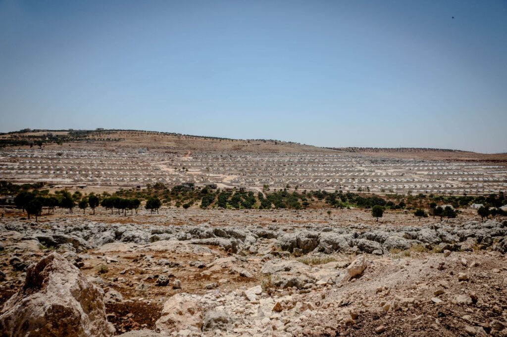 Expansive view of a refugee camp amidst a dry and rocky landscape in Idlib, Syria.