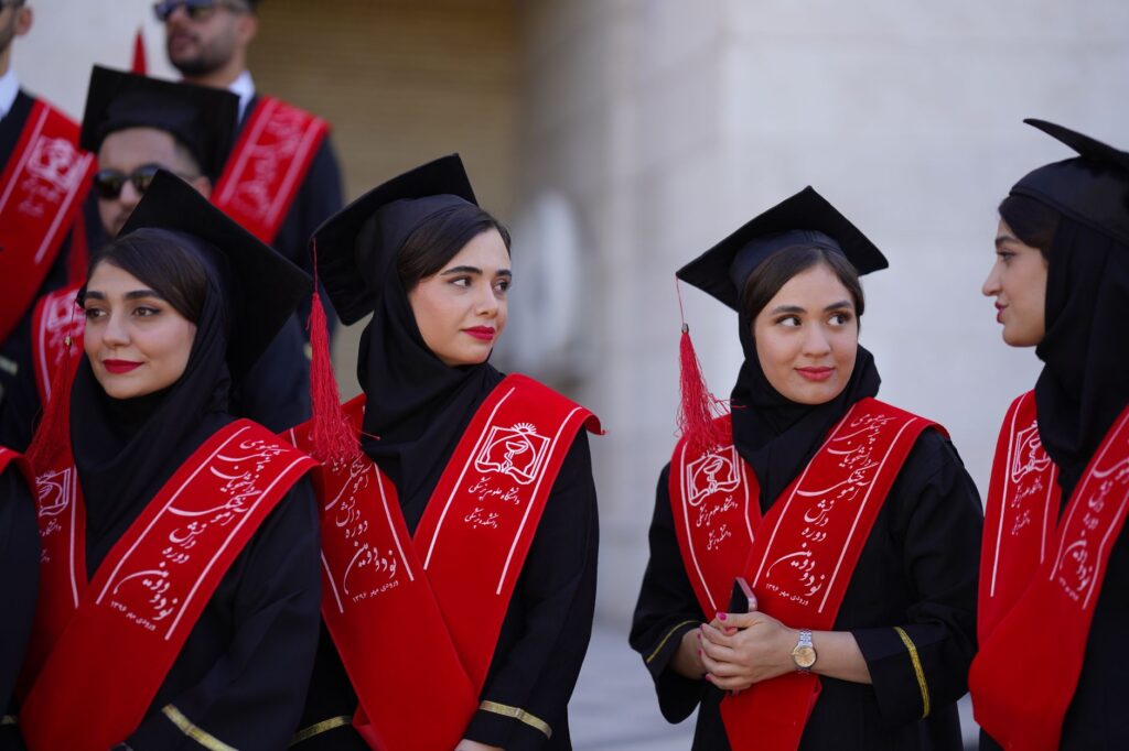 Group of Iranian female graduates in traditional attire celebrating outdoors.