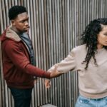 Disappointed African American male trying to stop unhappy ethnic girlfriend while having argument on street near wooden fence during breakup