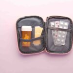 Open first aid kit with pill bottle, blister packs, and band-aids on a pastel background.