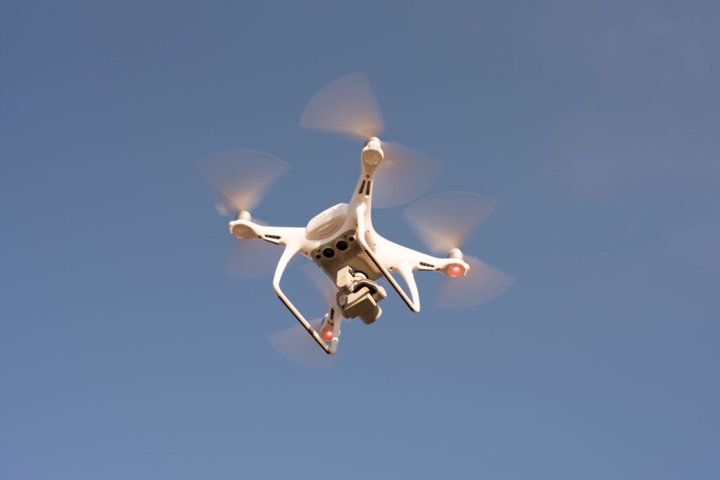 A white drone in flight against a clear blue sky, capturing aerial footage with precision.