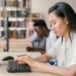 Students using computers in a library, focused on academic research and learning.
