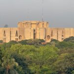 Aerial view of National Parliament House, Dhaka, surrounded by lush greenery under a clear sky.