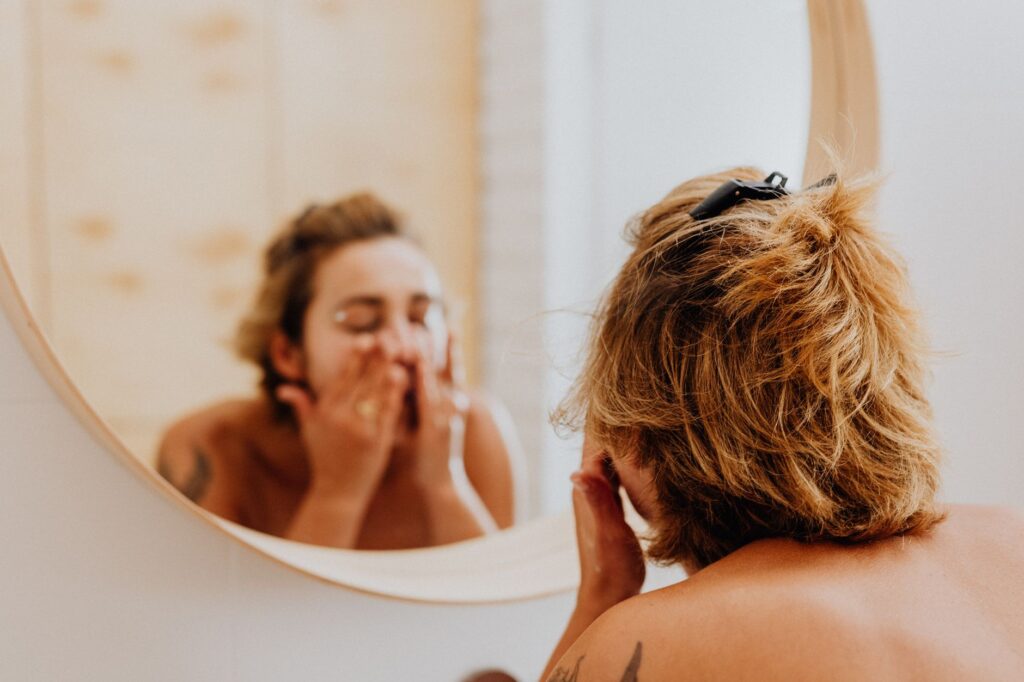 Young woman in bathroom applying facial products while looking in mirror, embracing self-care.