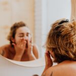 Young woman in bathroom applying facial products while looking in mirror, embracing self-care.