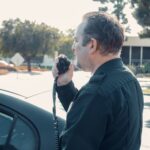 A police officer communicates using a radio outdoors during daytime patrol.