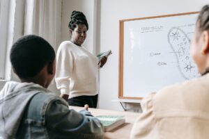 African American female teacher standing near whiteboard and explaining scheme to pupils during lesson in school