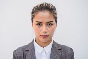 Portrait of a confident Asian woman wearing a plaid blazer and white shirt against a plain background.