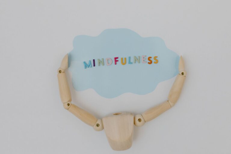 Wooden mannequin arms holding a blue cloud with 'Mindfulness' text, promoting self-awareness.