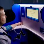 Man measuring blood pressure with a digital monitor at a self-service kiosk for telemedicine.