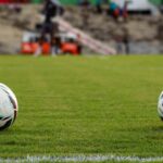 Two soccer balls resting on a vibrant green football field before a match begins.