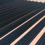 Aerial view of solar panels in a vast solar farm under bright sunlight.