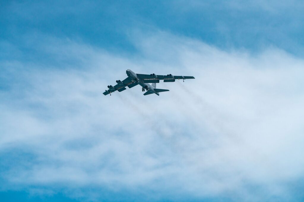 A B-52 Stratofortress aircraft soars through a clear blue sky on a sunny day.
