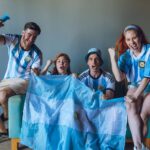 Group of excited Argentina soccer fans cheering with flag indoors.