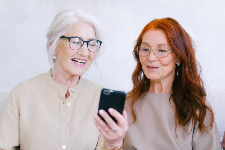 Happy senior women looking at screen of mobile phone while watching video through internet